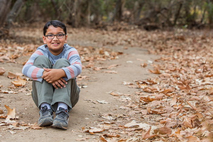 A young boy sitting among autumn leaves on a forest floor