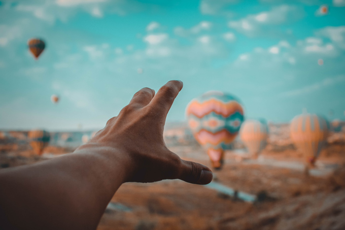 A forced perspective photo of a persons hand reaching toward hot air balloons using orange and teal color scheme