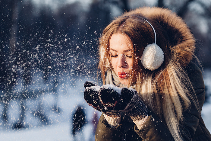 Close up winter portrait photography of a female model posing playfully in the falling snow