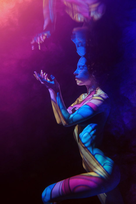 Artistic underwater photoshoot of a female model surrounded by colored light posing underwater
