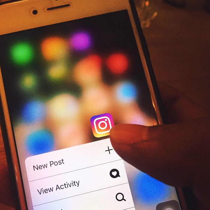 A persons hand pointing at an Instagram app on the screen of a smartphone.