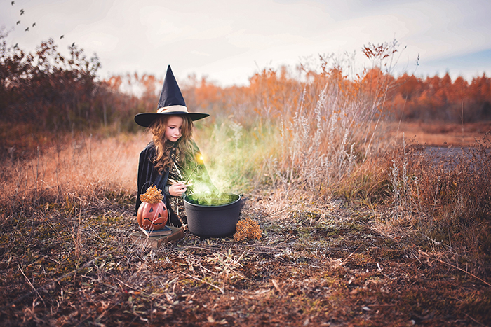 A little girl dressed as a witch. Her cauldron has been edited to look like there is a potion brewing inside it.