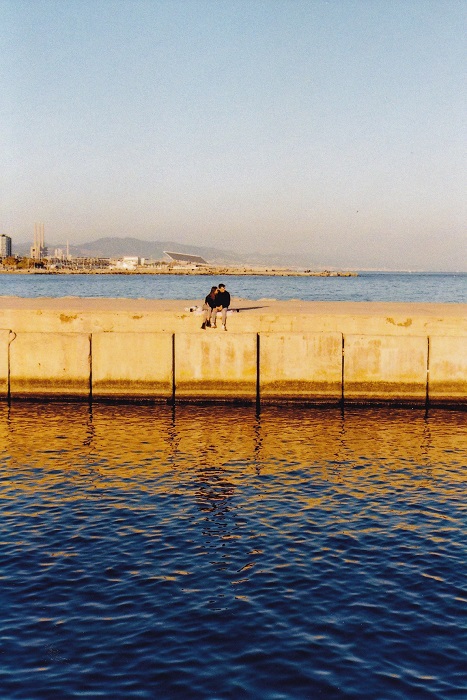 Couple sitting on a concrete pier above a blue sea