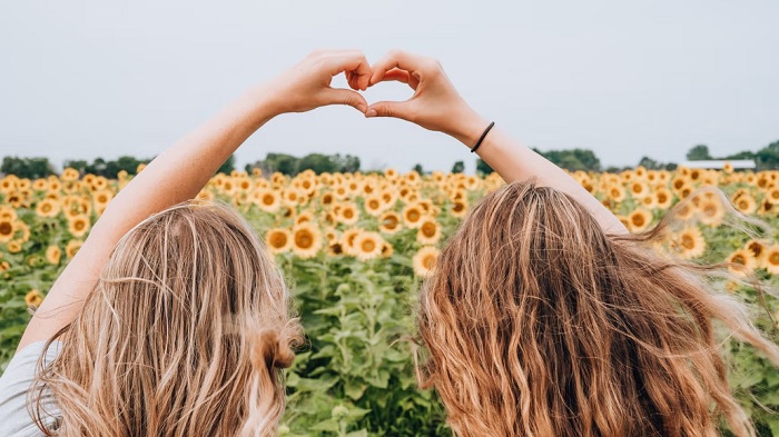 Two girls in a sunflower field making a hand heart