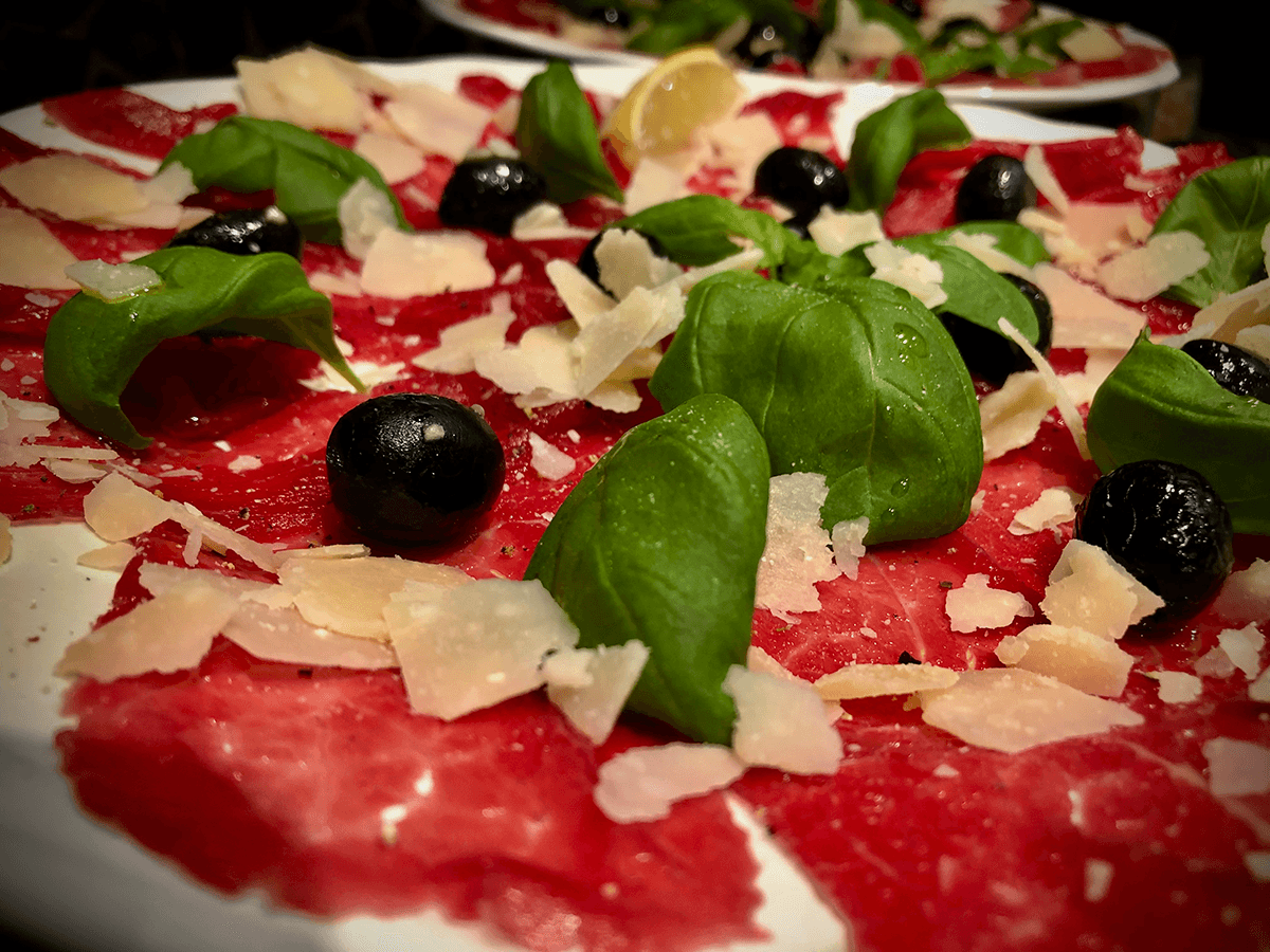 A close-up of beef carpaccio, fresh basil and parmesan cheese