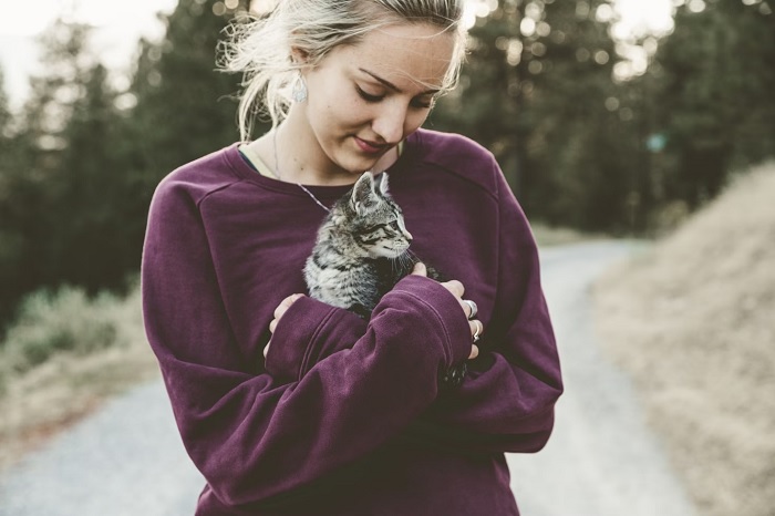 Woman holding a small cat in woodland road