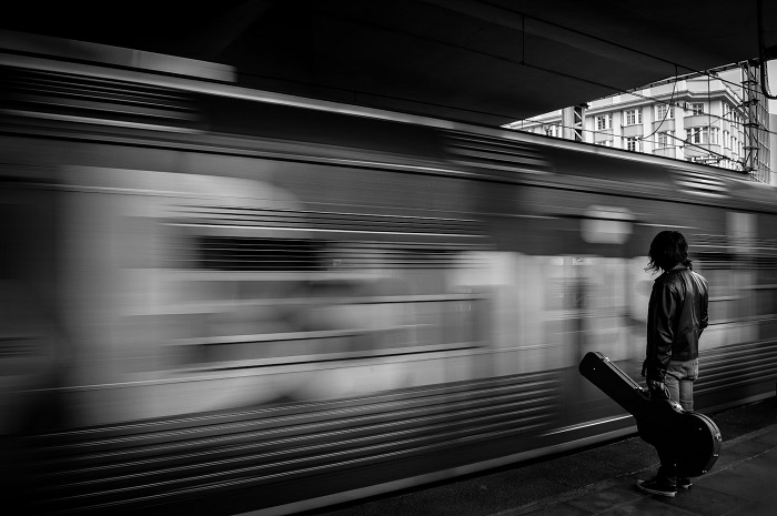 Man with guitar on station platform with train passing